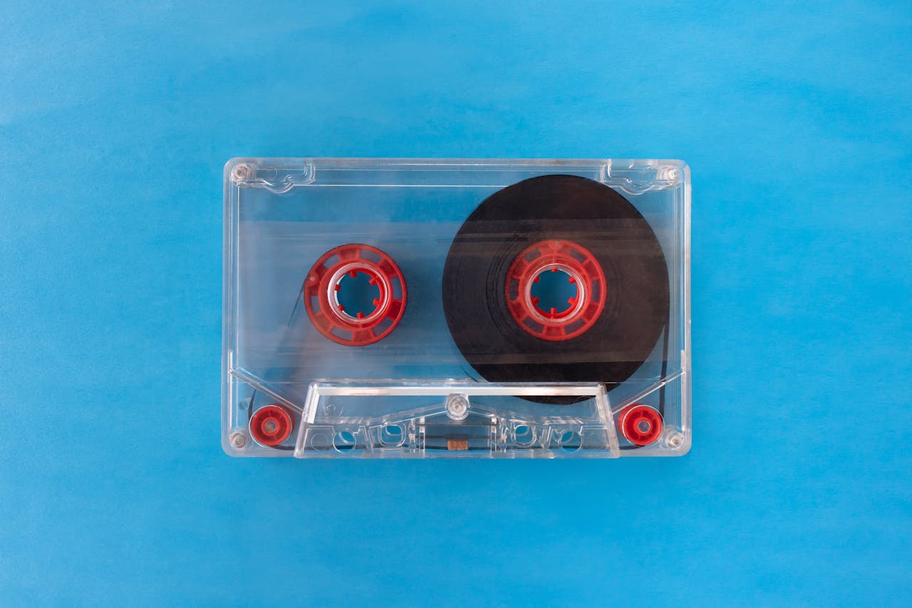 services-01 Vintage transparent cassette tape with red reels on a bright blue background.